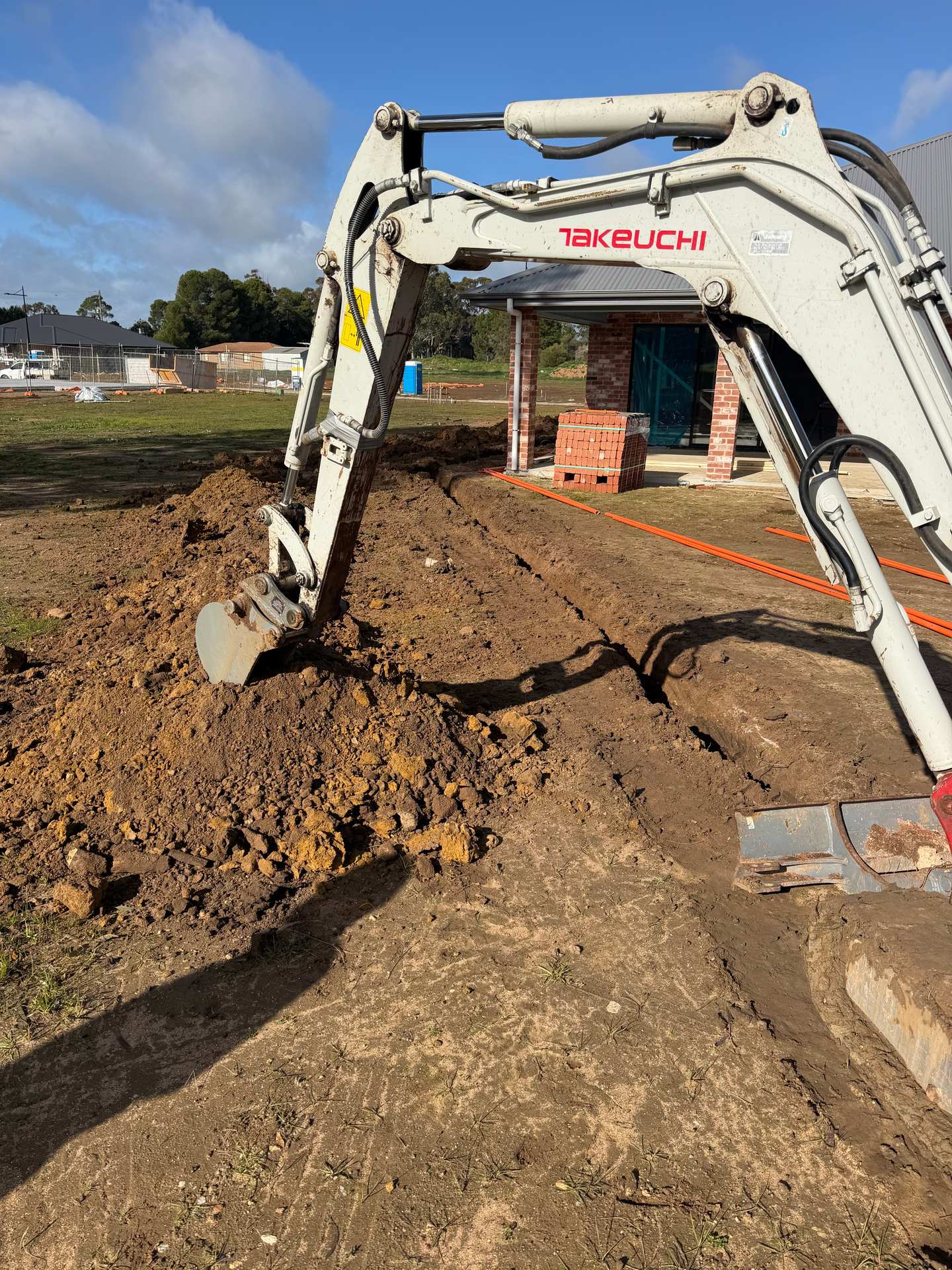 Excavator trenching for a sewer run beside a home